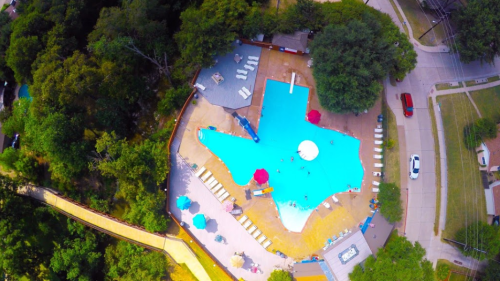 Aerial view of a large swimming pool surrounded by trees, lounge chairs, and colorful umbrellas.