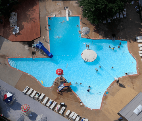 Aerial view of a large pool area with people swimming, slides, and lounge chairs around the water.