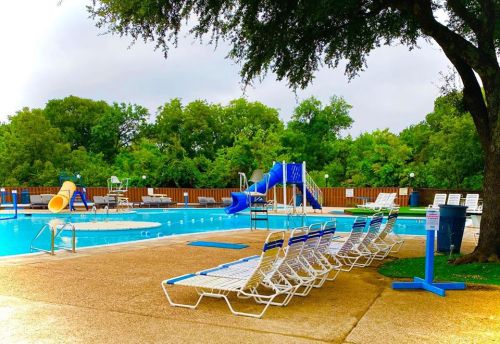 A swimming pool area with lounge chairs, a water slide, and trees in the background on a cloudy day.