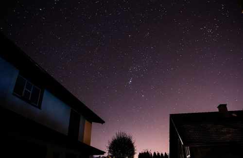 Starry night sky above silhouettes of houses, with a hint of purple and orange glow on the horizon.