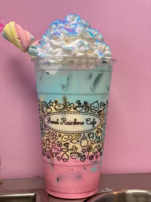 A colorful layered drink with whipped cream and a marshmallow on top, served in a decorative cup.