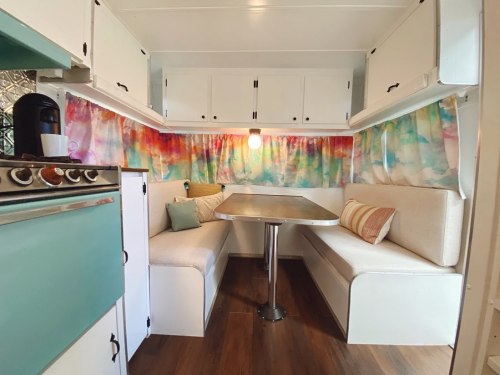 Cozy camper interior with colorful curtains, a dining table, and a kitchenette featuring a stove and coffee maker.
