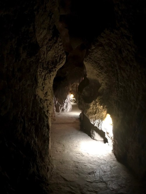 A dimly lit cave passage with rocky walls and soft light illuminating the path ahead.