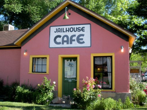 A colorful cafe building with a pink exterior, yellow trim, and a sign reading "Jailhouse Cafe." Flowers are in front.