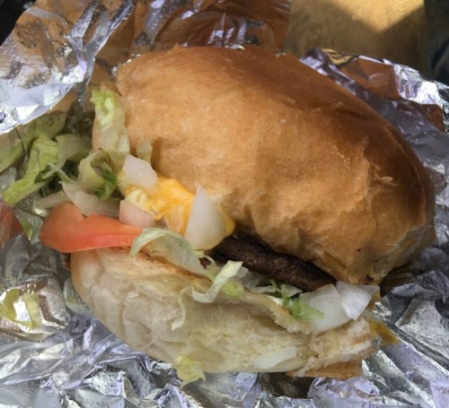 A close-up of a hamburger with lettuce, tomato, and cheese, wrapped in foil.