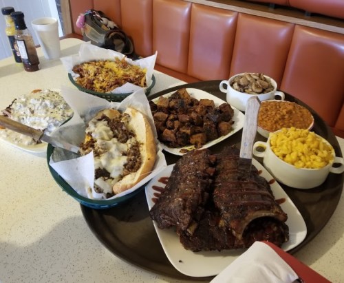A large platter of various barbecue dishes, including ribs, mac and cheese, baked beans, and sides, on a table.