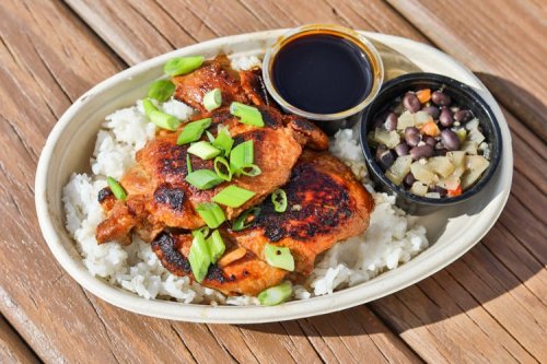 Grilled chicken on rice, topped with green onions, served with a side of black beans and sauce in small containers.