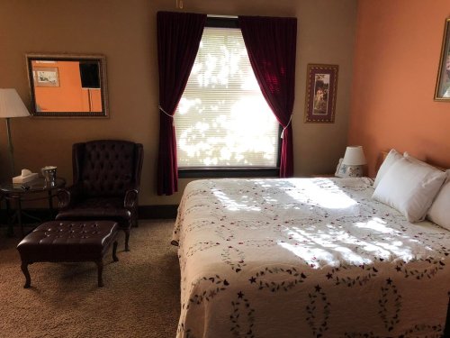 Cozy bedroom with a bed, armchair, and window, featuring warm colors and soft lighting.