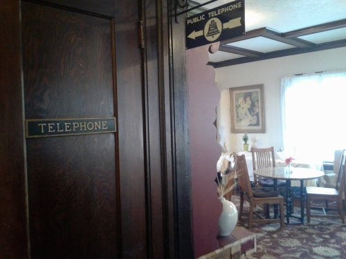 A wooden door labeled "Telephone" leads to a dining area with a table and chairs, featuring a cozy atmosphere.