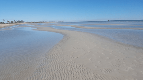 A serene beach scene with gentle waves, sandy shorelines, and a clear blue sky.