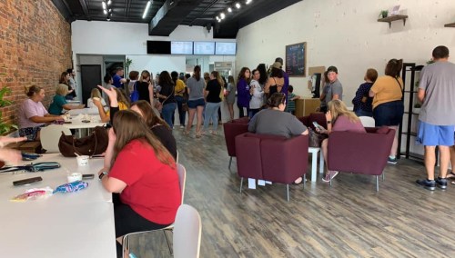 A busy café interior with a line of customers at the counter and people seated at tables and couches.