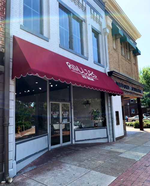 Exterior of Rollie's Ice Cream shop with a red awning, large windows, and an "Open" sign on a sunny day.