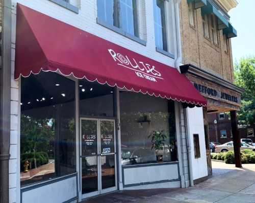Exterior of R. Liles Ice Cream shop with a red awning, next to a jewelry store, on a sunny day.