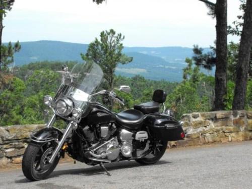 A black motorcycle parked on a scenic overlook with mountains and trees in the background.