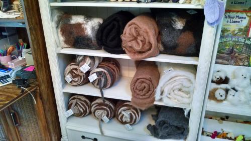 A display of neatly rolled wool blankets in various colors on a shelf, with tags visible on some.
