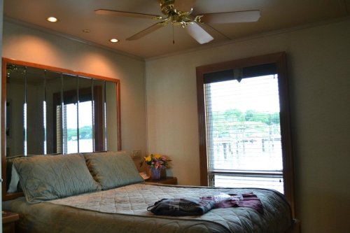 Cozy bedroom with a ceiling fan, large window, and a bed adorned with a quilt, overlooking a scenic view.