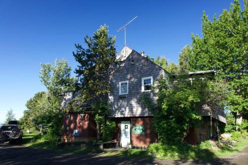 A rustic two-story building surrounded by trees and greenery under a clear blue sky.