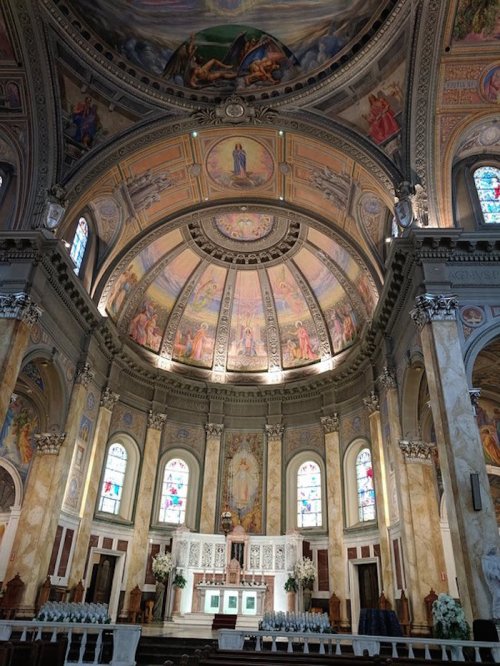 Interior of a grand church featuring a beautifully painted dome, stained glass windows, and an ornate altar.