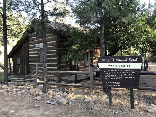 Historic cabin in Prescott National Forest, with a sign for Palace Station and surrounded by trees and rocky terrain.