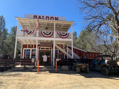 A rustic saloon building with a second floor, surrounded by trees and off-road vehicles, decorated for a celebration.