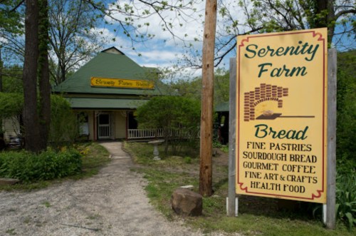 A quaint farm store with a sign advertising bread, pastries, and health food, surrounded by greenery.