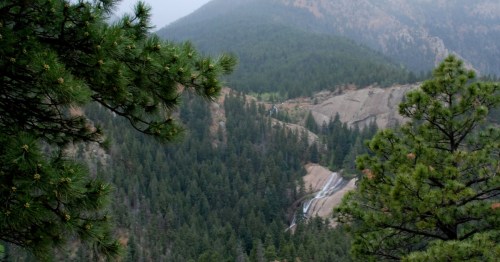 Distant view of Seven Falls in Colorado Springs, CO, framed by evergreen trees with mountains beyond