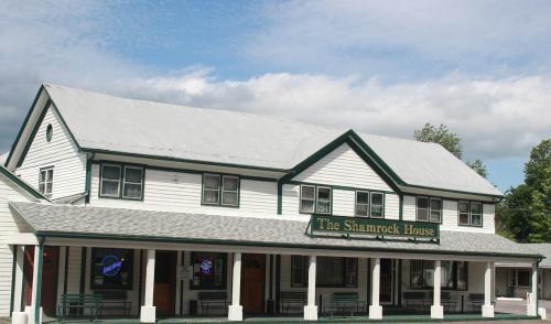 A two-story white building with green trim, featuring a sign that reads "The Shamrock House" and a blue sky above.