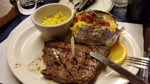 A plate with a grilled steak, a baked potato topped with cheese and bacon, and a side of corn.