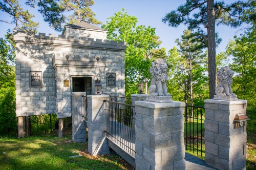 A stone castle-like structure with lion statues at the entrance, surrounded by greenery and trees.