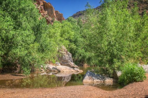 A serene river scene surrounded by lush greenery and rocky formations under a clear blue sky.