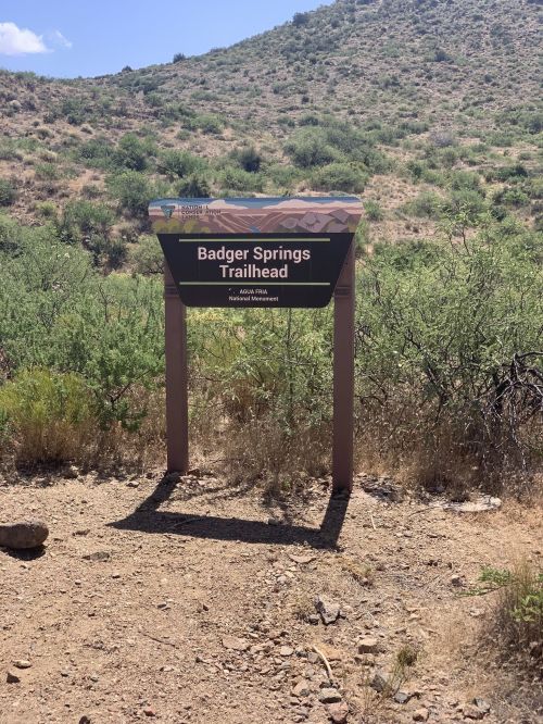Sign for Badger Springs Trailhead in a desert landscape with shrubs and hills in the background.