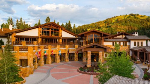 A scenic lodge entrance surrounded by trees and mountains, featuring flags and a welcoming pathway.