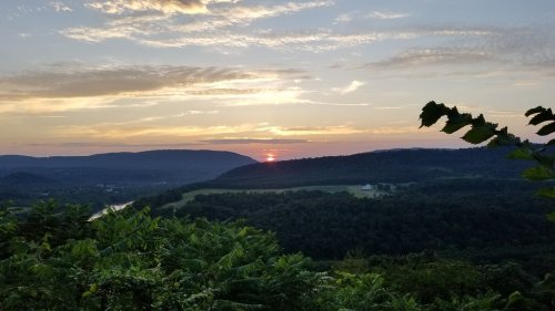 A scenic sunset over rolling hills, with vibrant clouds and a lush green foreground.