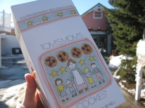 A hand holds a box of "Tom's Mom's Cookies," featuring a colorful illustration of a family and cookies on the packaging.