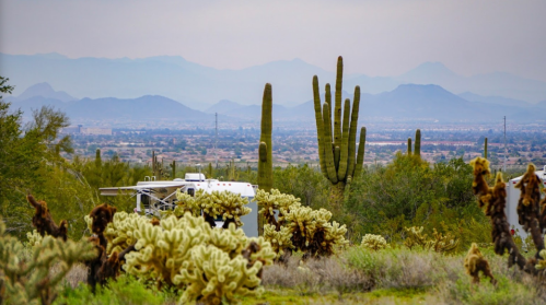 A desert landscape featuring cacti, mountains in the background, and a white RV among the vegetation.