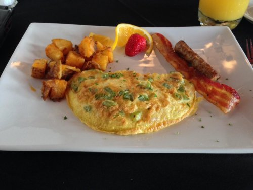 A plate with a vegetable omelet, crispy bacon, sausage, seasoned potatoes, and a lemon and strawberry garnish.
