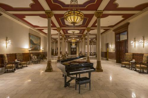 Elegant lobby featuring a grand piano, ornate chandeliers, and plush seating against marble flooring and decorative columns.