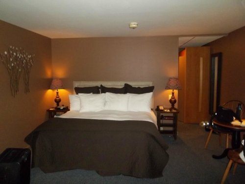 Cozy hotel room featuring a large bed, bedside lamps, and a small dining table in a warm-toned setting.