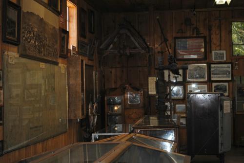 Interior of a museum featuring wooden walls, historical artifacts, maps, and framed photographs. Display cases in foreground.