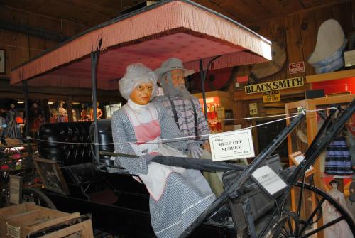 A vintage horse-drawn carriage with two lifelike mannequins dressed in old-fashioned attire sitting inside.