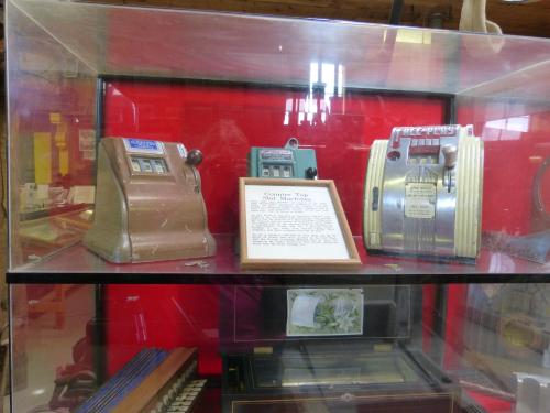 Three vintage cash registers displayed in a glass case, with a sign and a decorative card in front.