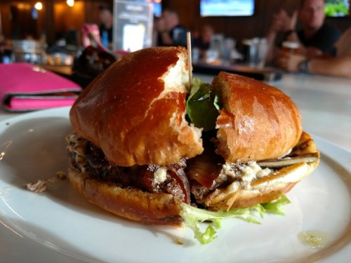 A close-up of a halved burger on a plate, featuring lettuce and meat, with a blurred bar background.