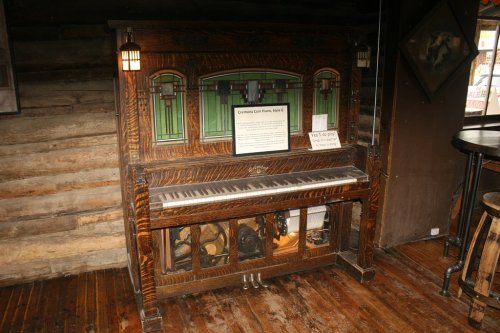 An antique coin-operated piano with stained glass details, set against a rustic wooden wall.