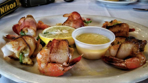 A plate of shrimp wrapped in bacon, garnished with lemon slices and a small cup of dipping sauce.