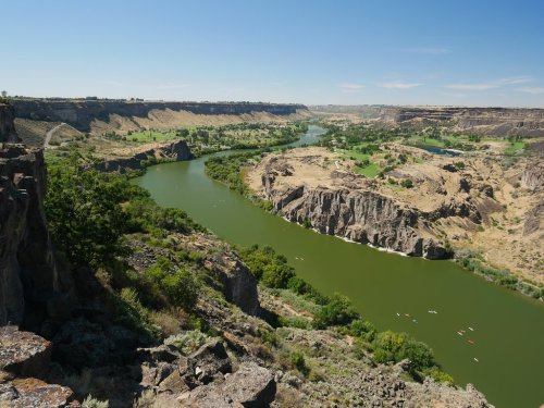 A scenic view of a winding river surrounded by cliffs and lush greenery under a clear blue sky.