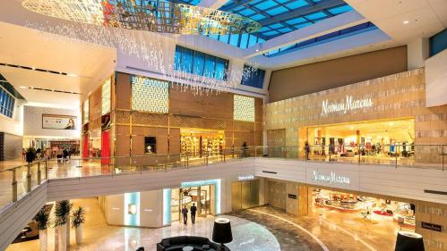 Interior view of a modern shopping mall with high ceilings, elegant decor, and various retail stores.