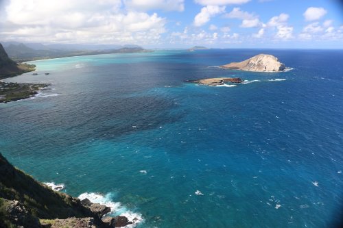 A scenic view of turquoise waters and a distant island under a partly cloudy sky.