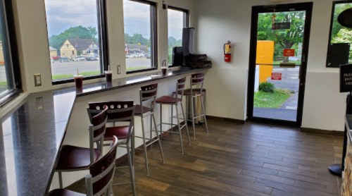 A bright cafe interior with tall chairs at a counter, large windows, and a door leading outside.
