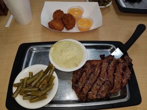 A plate with grilled steak, green beans, creamy grits, and a side of cheese dip with fried bites in the background.