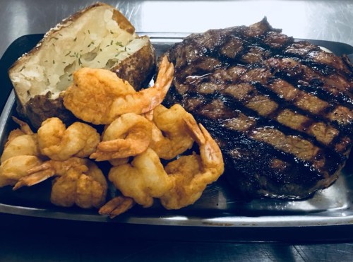 A plated meal featuring a grilled steak, crispy shrimp, and a baked potato with herbs.